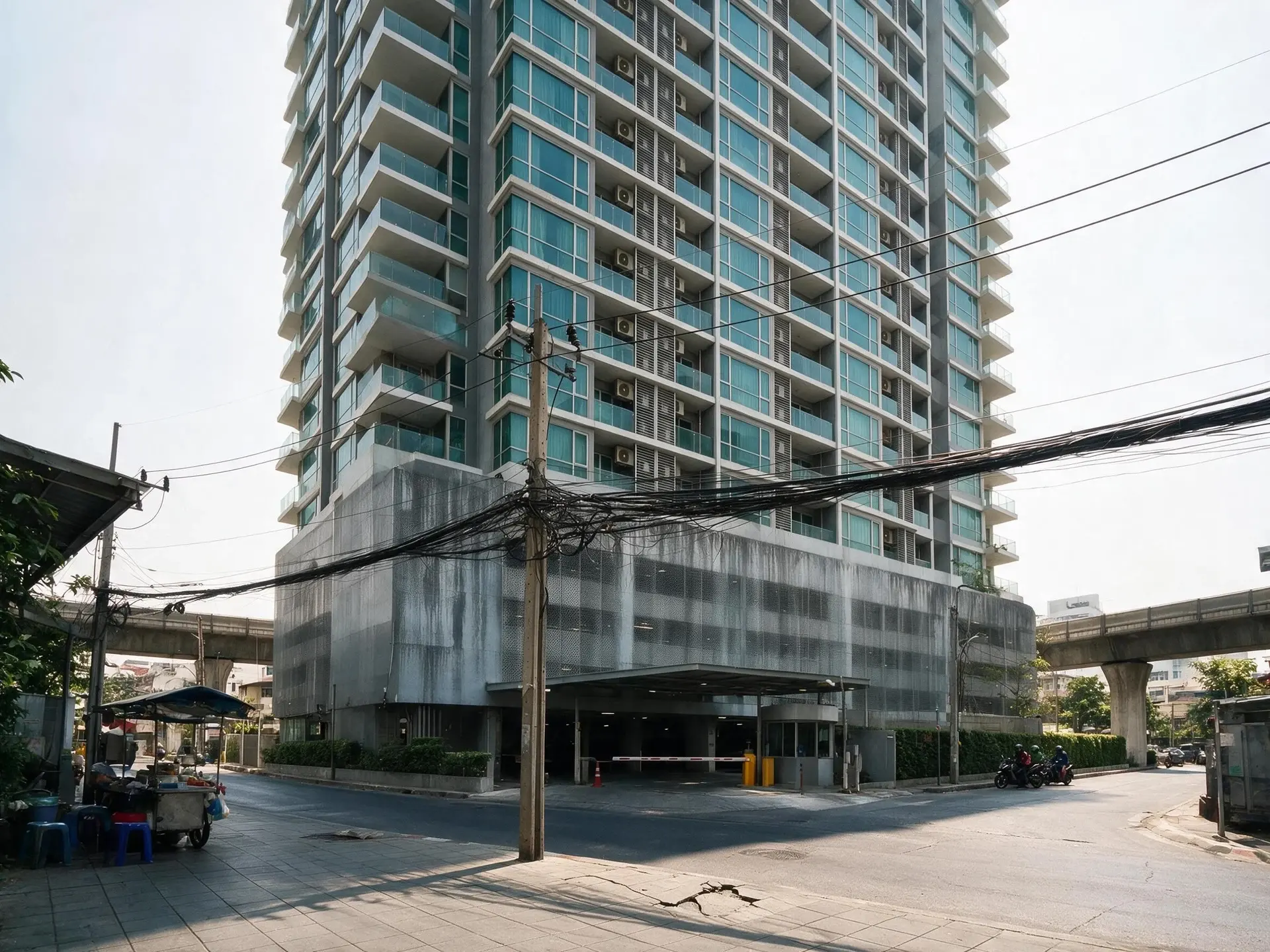 Before and after of a sukhumvit condo tower shot from a footpath too close to it, so the building leans back and the frame rolls — enhanced by Plotpane