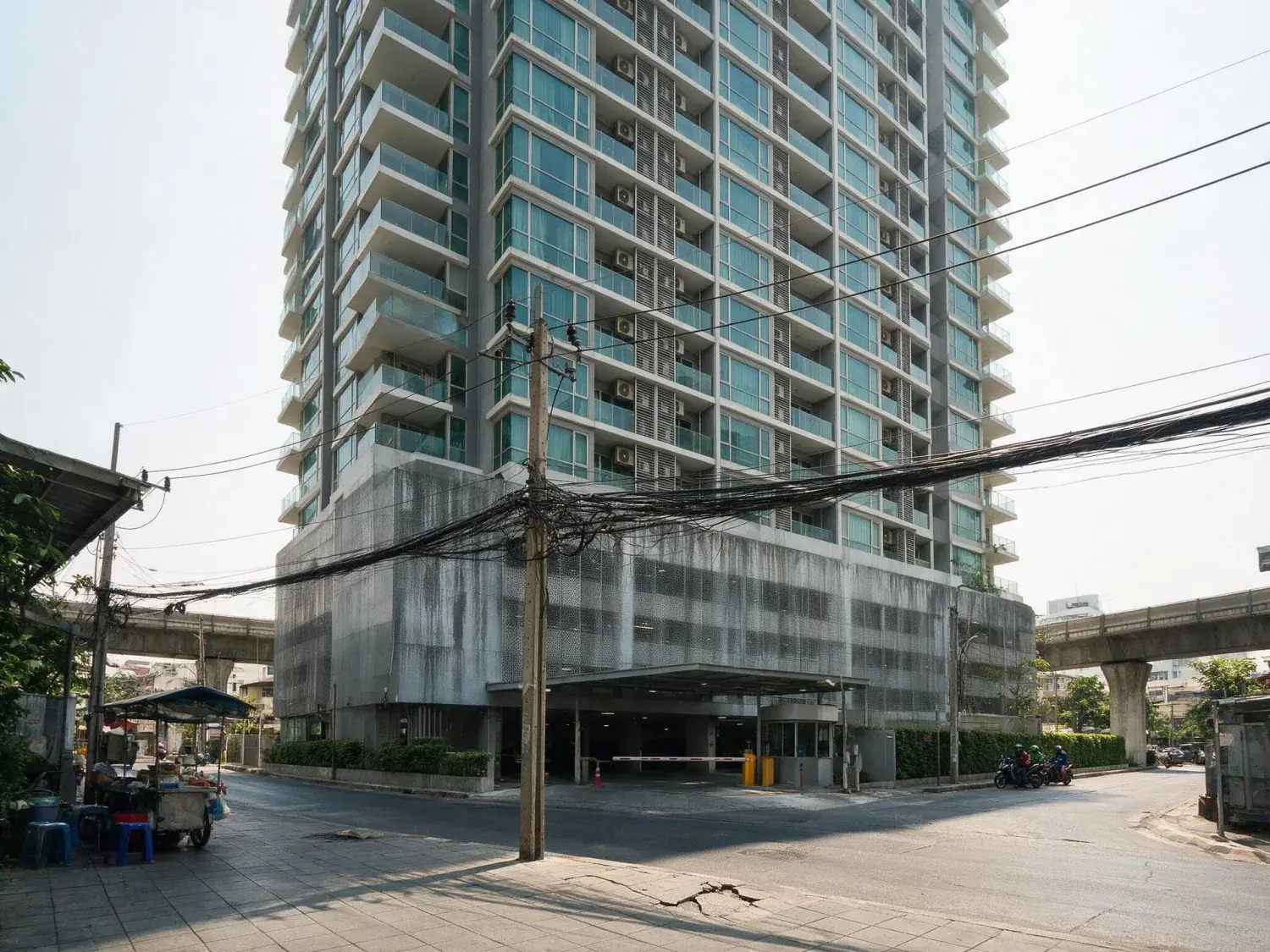 Before and after of a sukhumvit condo tower shot from a footpath too close to it, so the building leans back and the frame rolls — original listing photo before editing