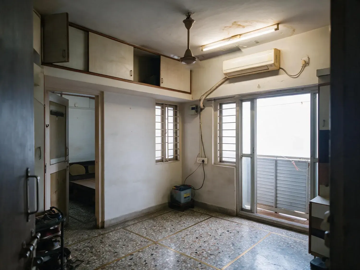 Before and after of a bandra one-bedroom photographed on a phone against a monsoon-grey window, so the room sits dark and the tube light throws everything green — enhanced by Plotpane