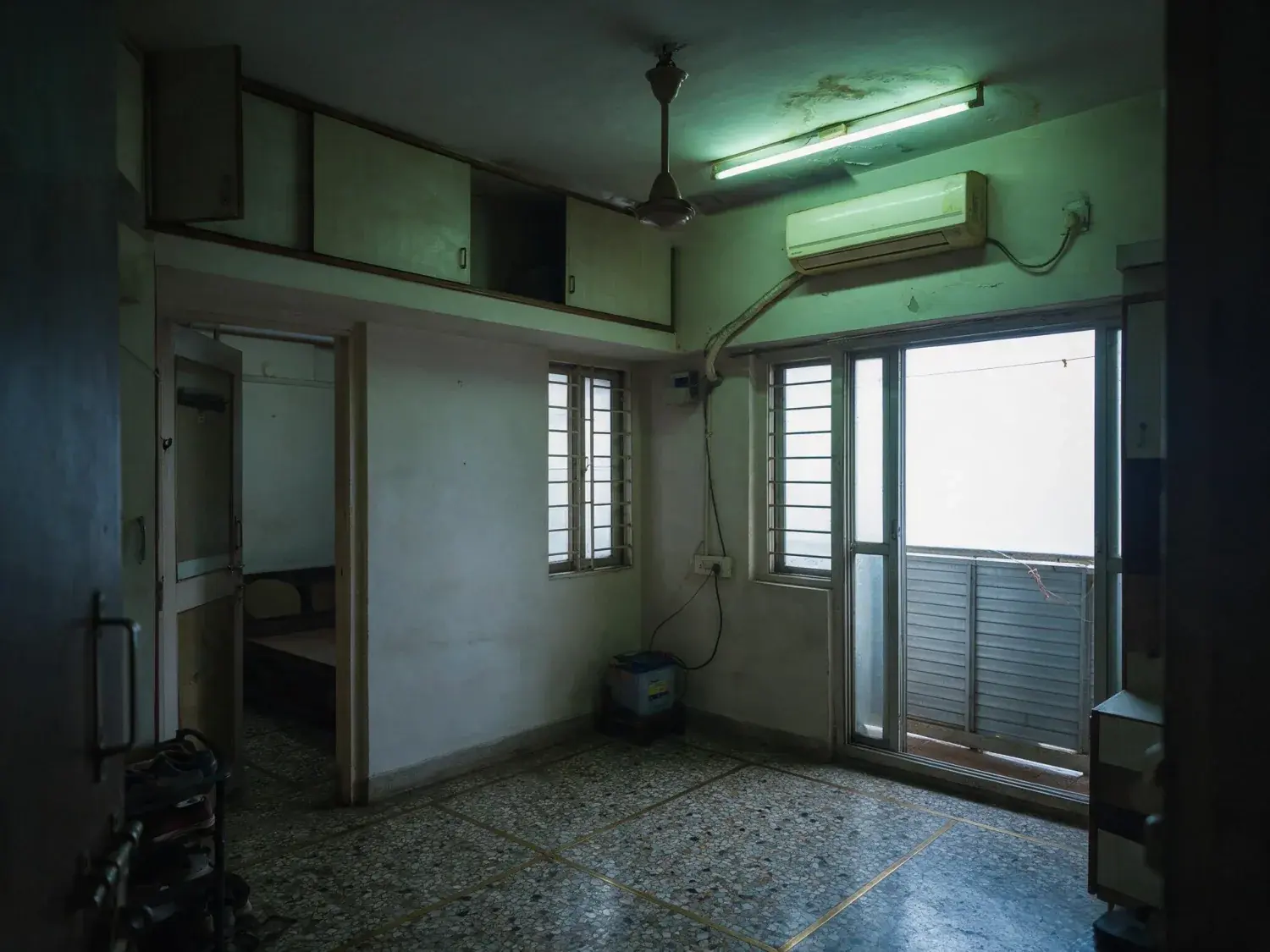 Before and after of a bandra one-bedroom photographed on a phone against a monsoon-grey window, so the room sits dark and the tube light throws everything green — original listing photo before editing