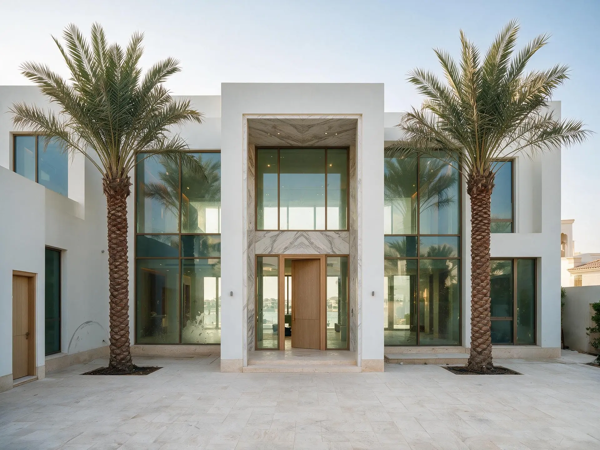 Before and after of the front elevation from the driveway, the two-storey entrance portal centred, mature palms either side, the motor court in pale stone, one of ten frames from a single Palm Jumeirah villa shoot in Dubai.