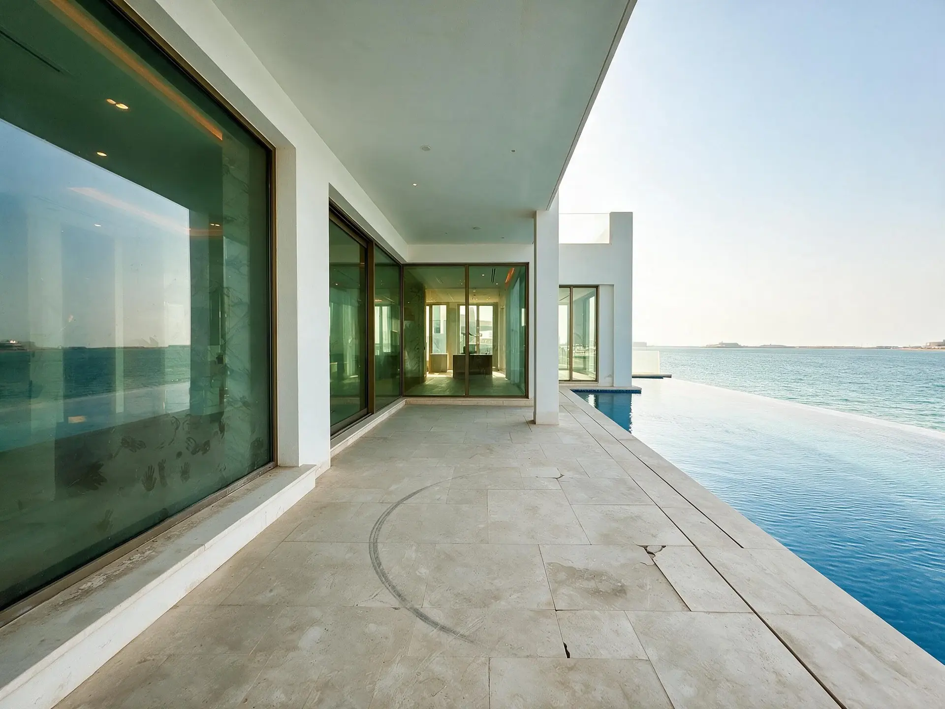 Before and after of the pool terrace from the far end, the infinity edge running to the Gulf, sun loungers absent, the villa behind on the left, one of ten frames from a single Palm Jumeirah villa shoot in Dubai.