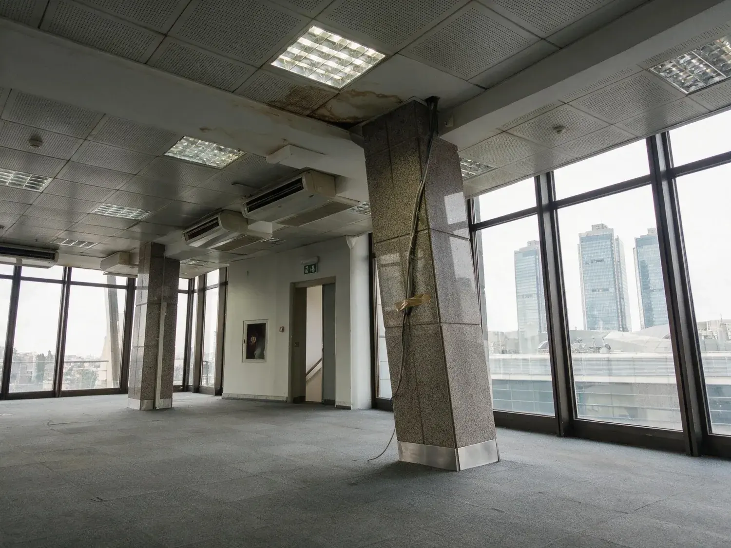Before and after of a levent plaza floor photographed hand-held and tipped back, so every column and mullion leans in — original listing photo before editing