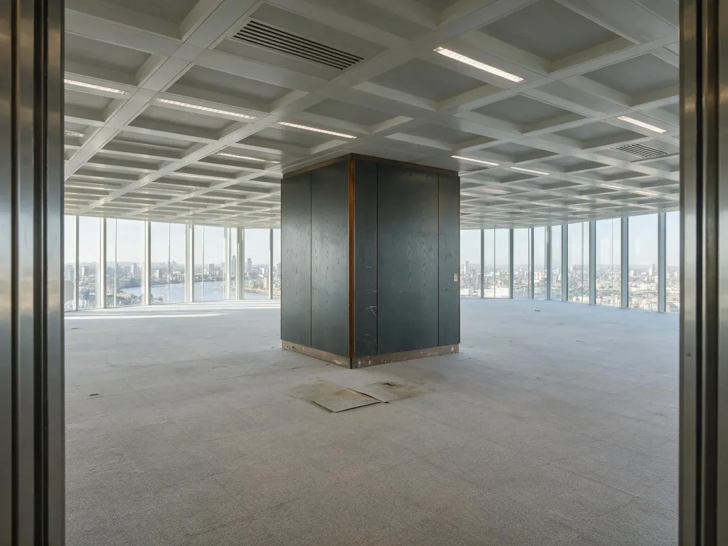 Before and after of a completely empty canary wharf office floorplate is staged as a working tenant fit-out, framing the existing thames view — original listing photo before editing