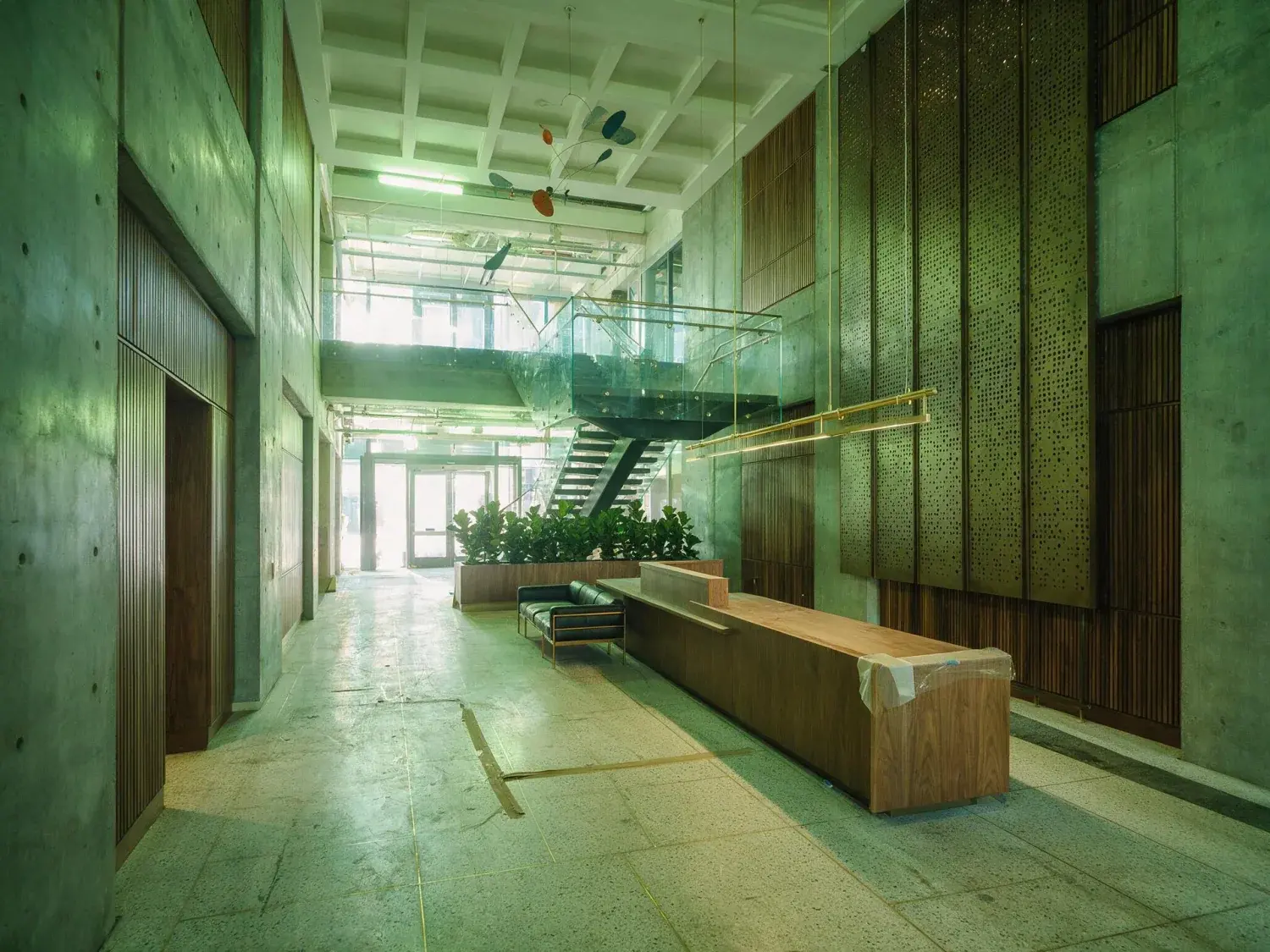 Before and after of a soma tech-hq arrival lobby recovers its true depth of concrete, walnut, and natural light from a muddy pre-construction capture — original listing photo before editing