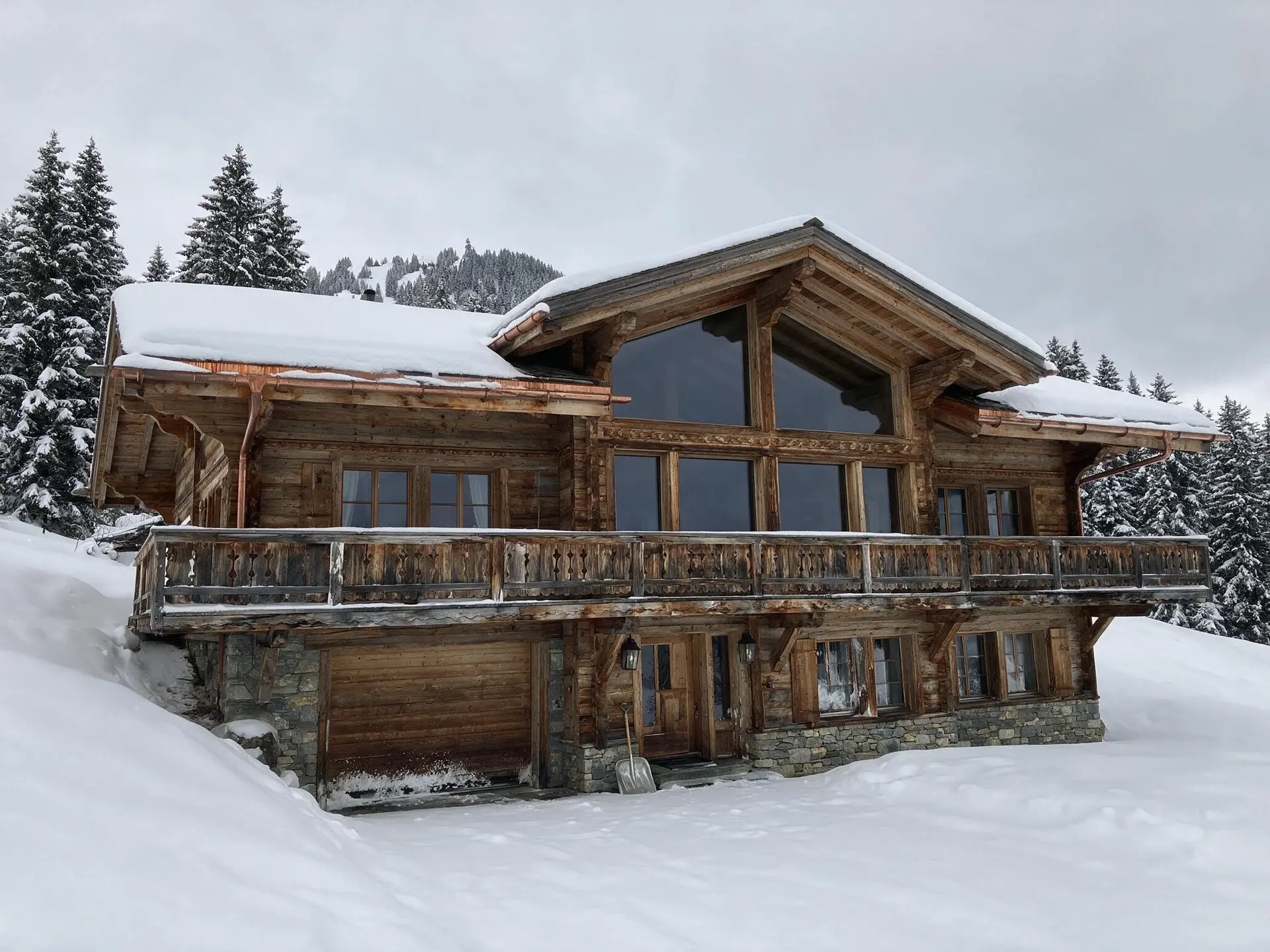 Before and after of a larch-clad Gstaad chalet in the Swiss Alps converted to blue-hour dusk. — original listing photo before editing