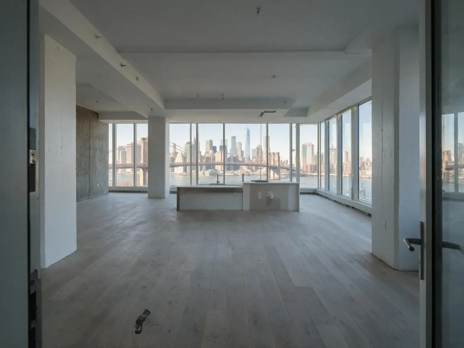 Before and after of a raw-concrete dumbo presales condo unit is renovated into a finished listing-ready residence, framing the existing bridge-and-skyline view — original listing photo before editing