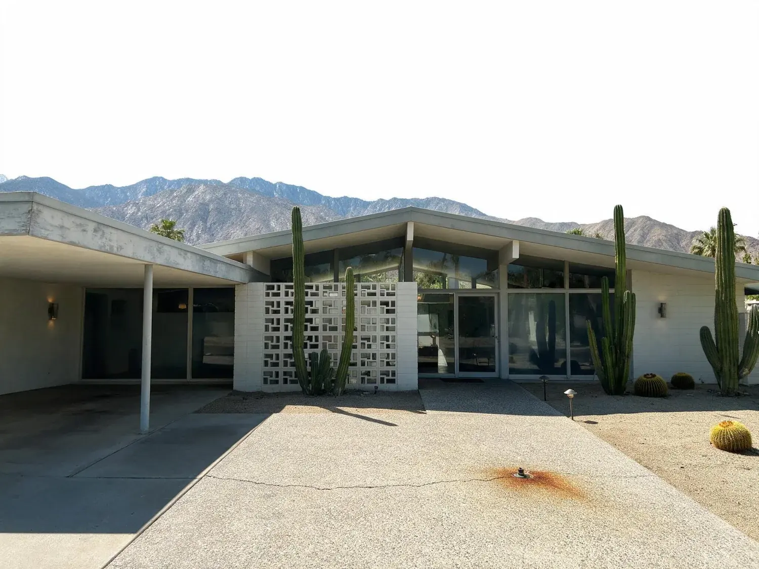 Before and after of a butterfly-roof palm springs desert modern home shifts from hot flat midday to an iconic magenta-mountain twilight — original listing photo before editing