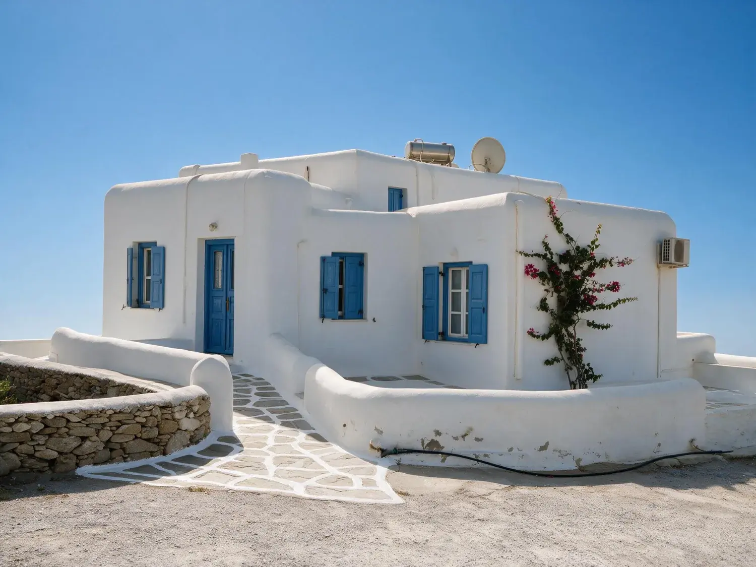 Before and after of a mykonos villa shot under a hazy white summer sky, with only the sky replaced — enhanced by Plotpane