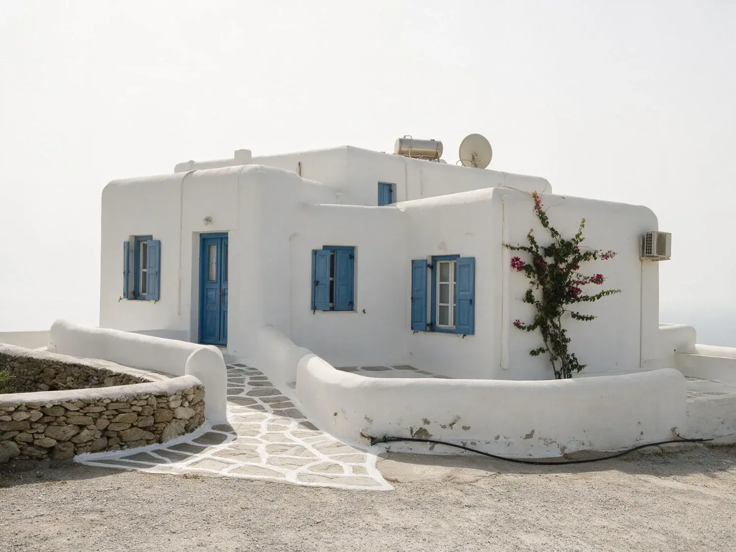 Before and after of a mykonos villa shot under a hazy white summer sky, with only the sky replaced — original listing photo before editing