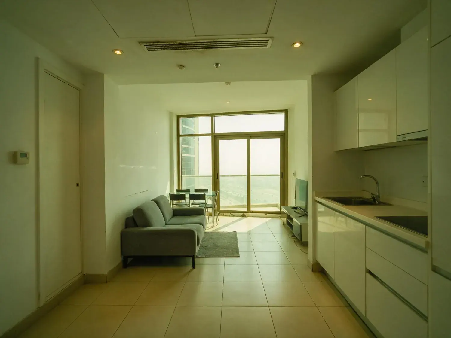 Before and after of a landlord-furnished downtown dubai one-bed shot into the window, so the room sits dark and the glass is blown out — original listing photo before editing