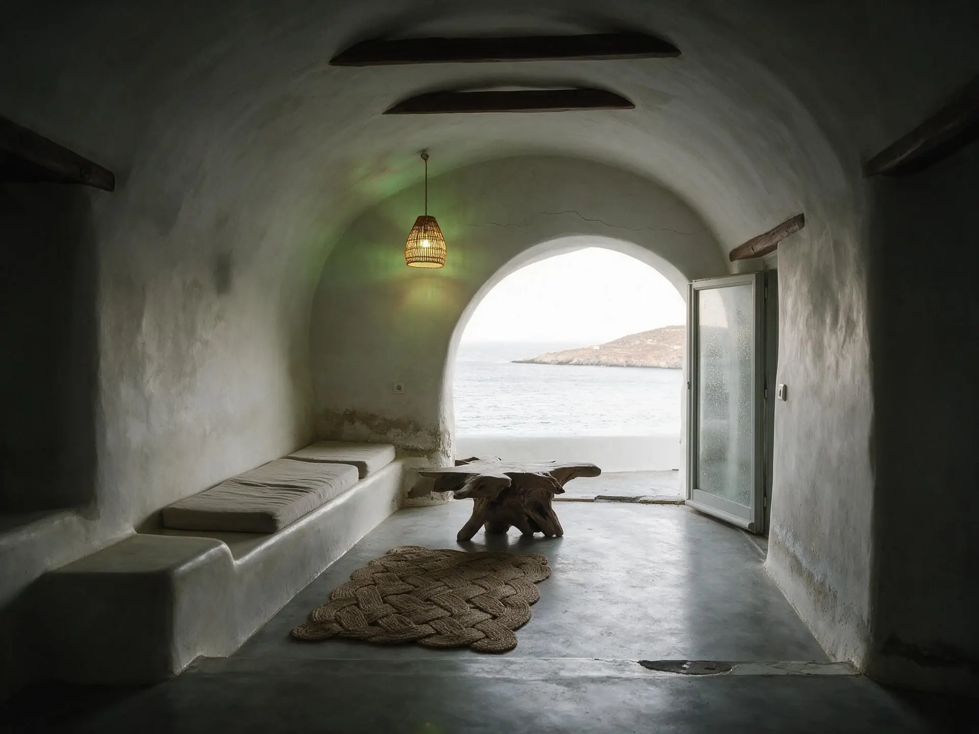 Before and after of a whitewashed cave-house living room above Psarou bay in Mykonos. — original listing photo before editing