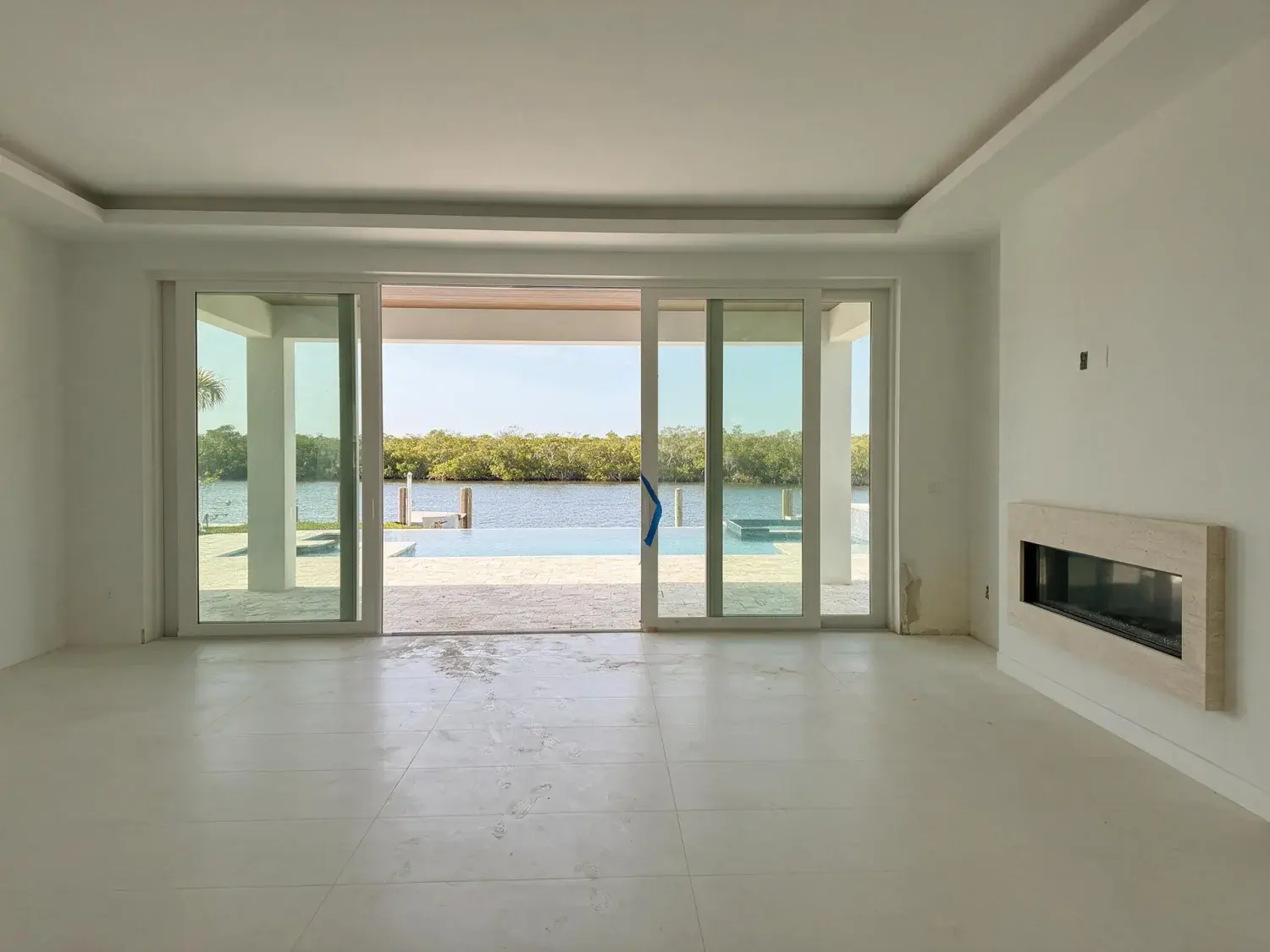 Before and after of empty port royal waterfront contemporary great room virtually staged with coastal-modern furniture while preserving the gordon pass water view — original listing photo before editing