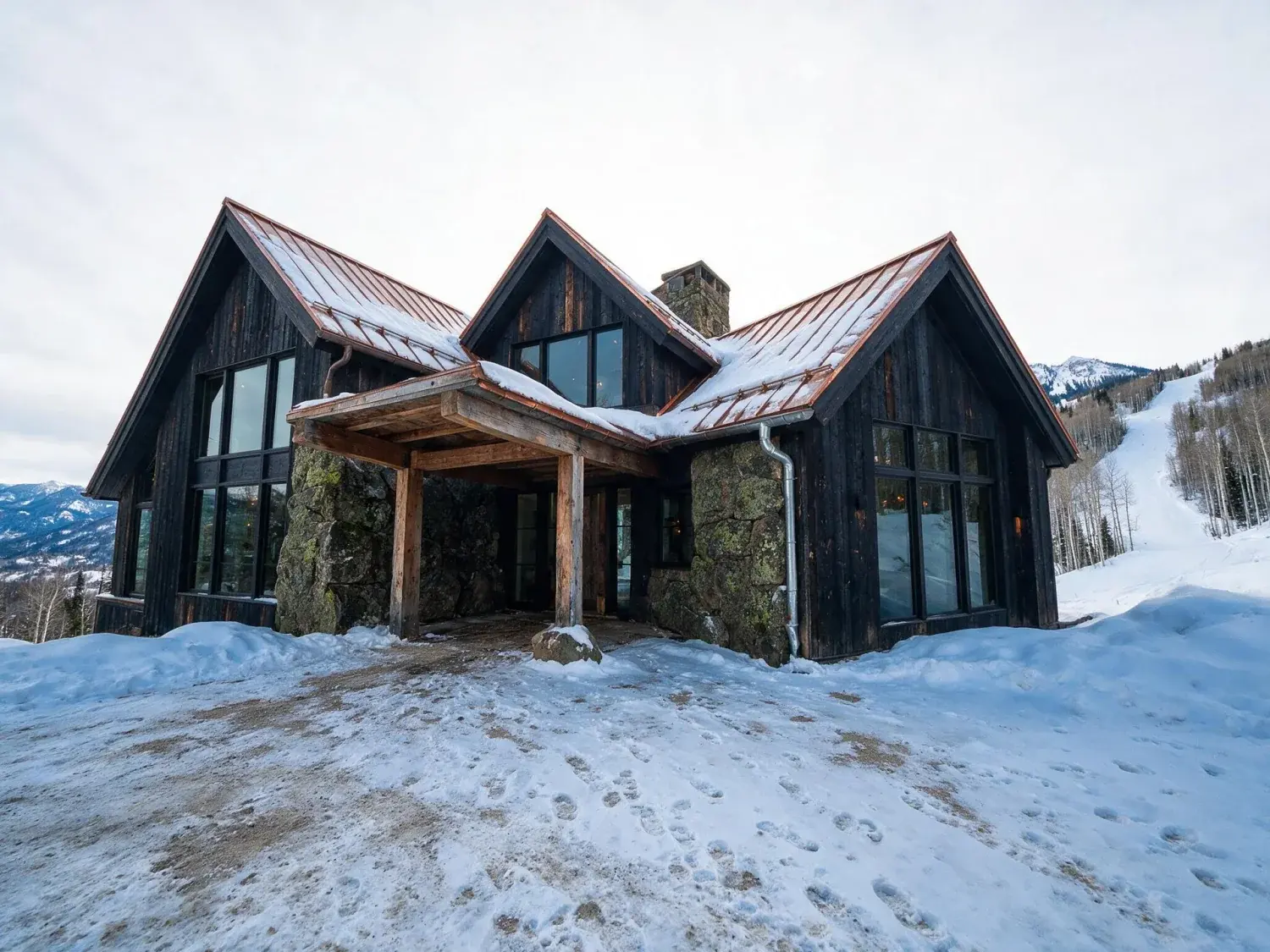 Before and after of a red mountain ski estate of blackened timber and drystone rises from powder snow, the existing rockies behind it resolving into crisp alpine clarity — original listing photo before editing