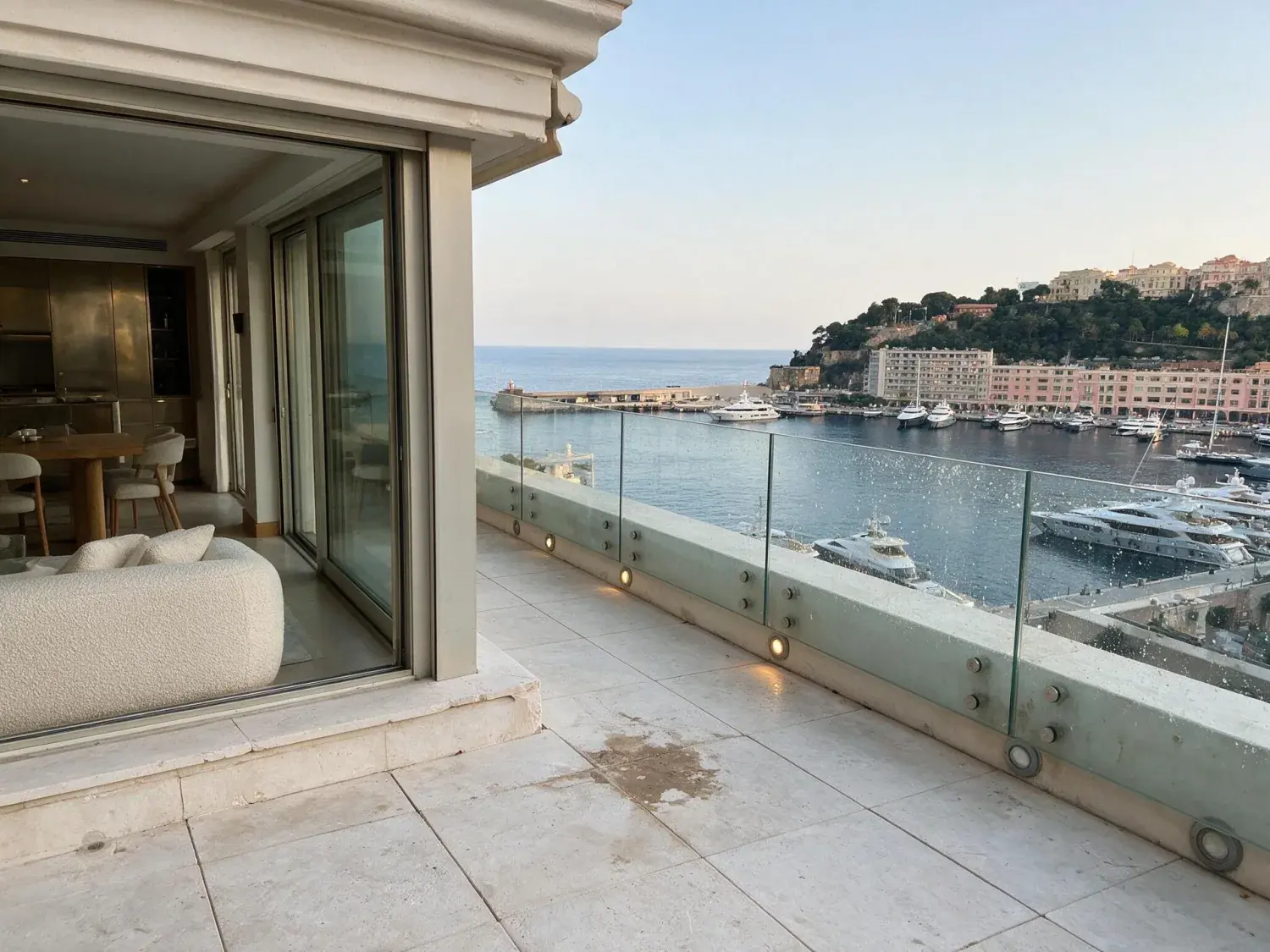 Before and after of a sleek monaco apartment terrace faces the existing port hercules yachts as the riviera dusk lights their decks into a constellation — original listing photo before editing