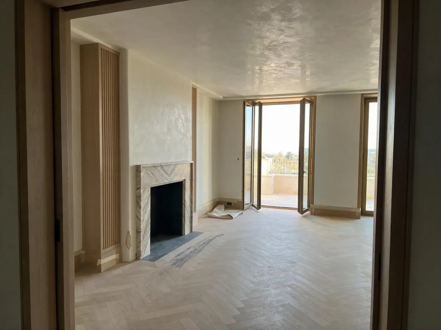Before and after of an empty rosewood signature suite is dressed into a residential club salon, its terrace doors flung open to a distant existing view — original listing photo before editing