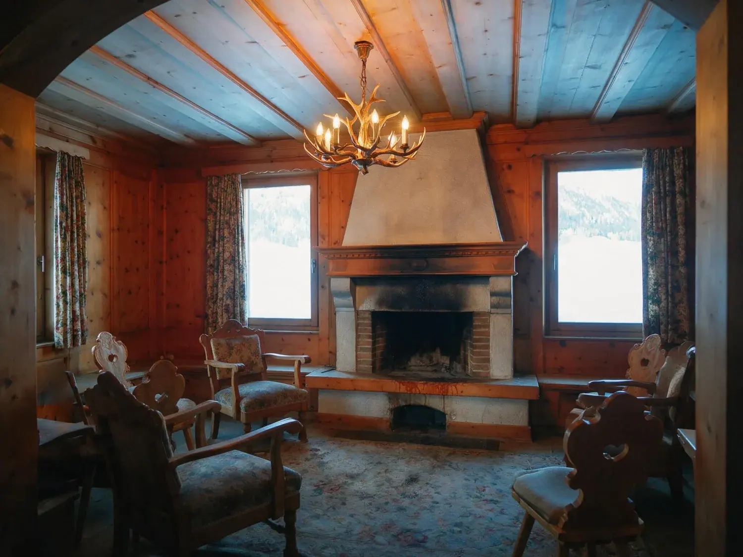 Before and after of a dated st moritz chalet salon is reimagined as a contemporary alpine sanctuary of blackened timber, raw stone and ivory shearling — original listing photo before editing