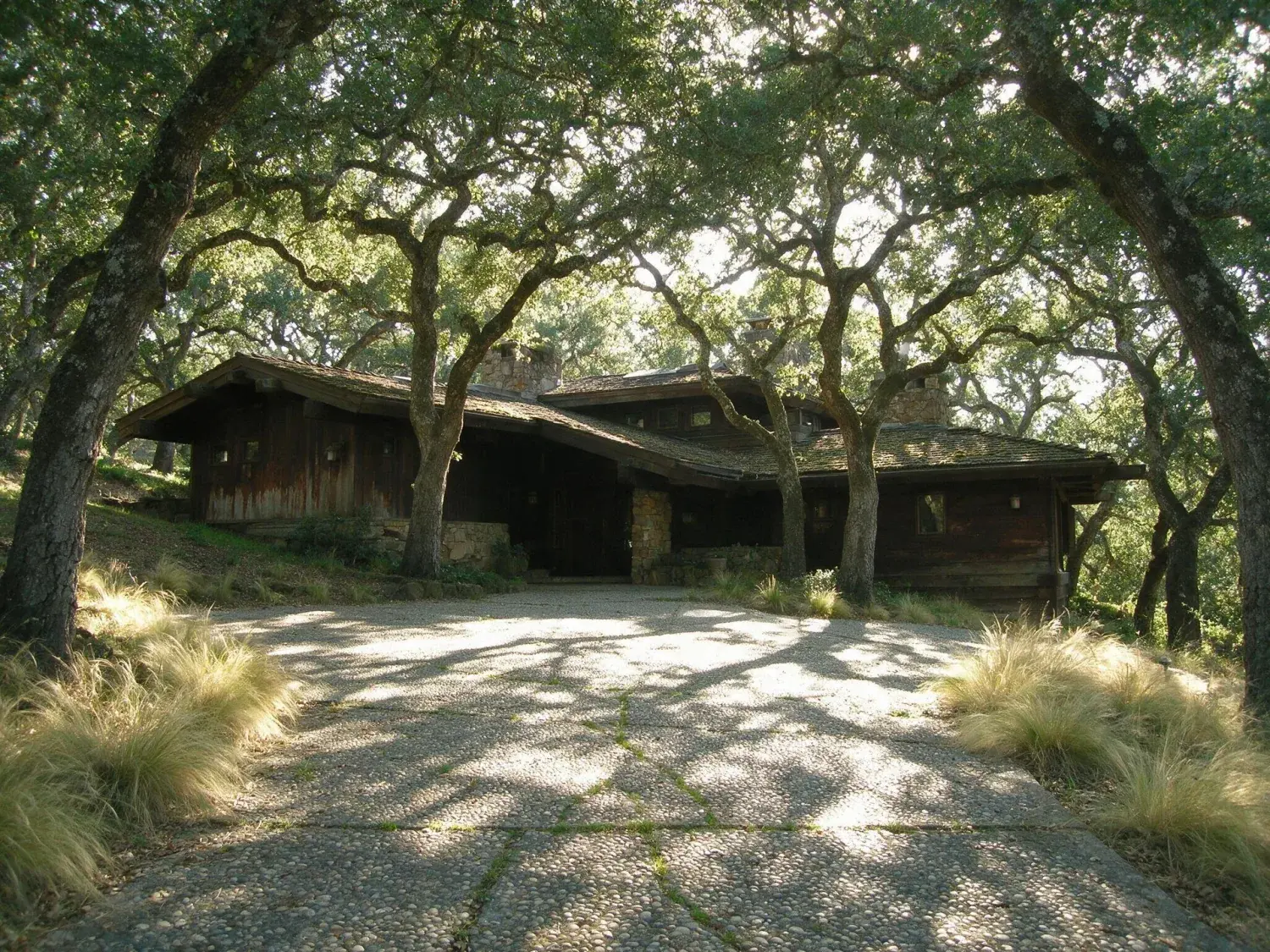 Before and after of a dated woodside estate of stone and oak is reimagined as a tadao ando concrete-and-glass pavilion floating among centennial live oaks — original listing photo before editing