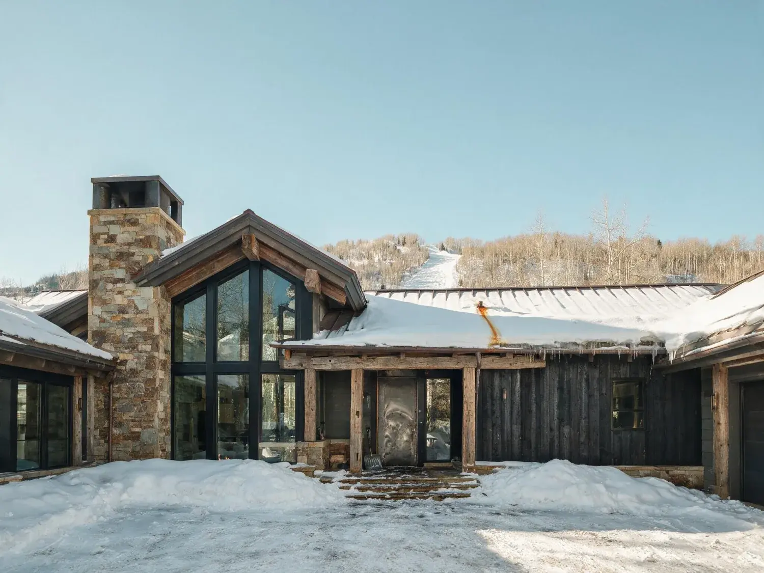 Before and after of an aspen ski-lodge great room swaps a flat bluebird afternoon sky for a dramatic post-storm dusk above ajax mountain — original listing photo before editing
