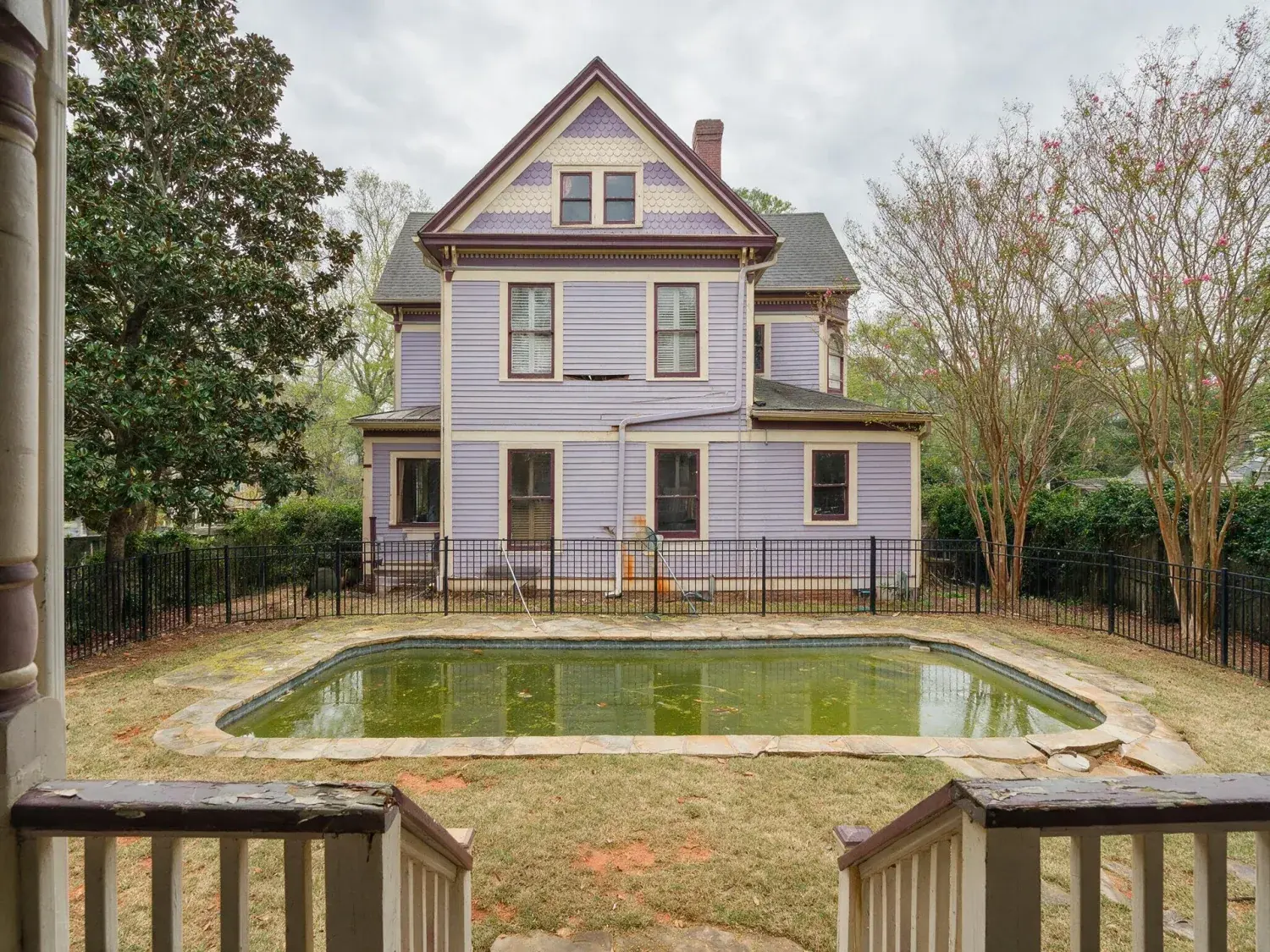 Before and after of a restored 1890s inman park queen anne victorian with an algae-clouded gunite pool and pollen-yellowed lawn — reborn as an emerald zoysia carpet and resort-blue pool — original listing photo before editing