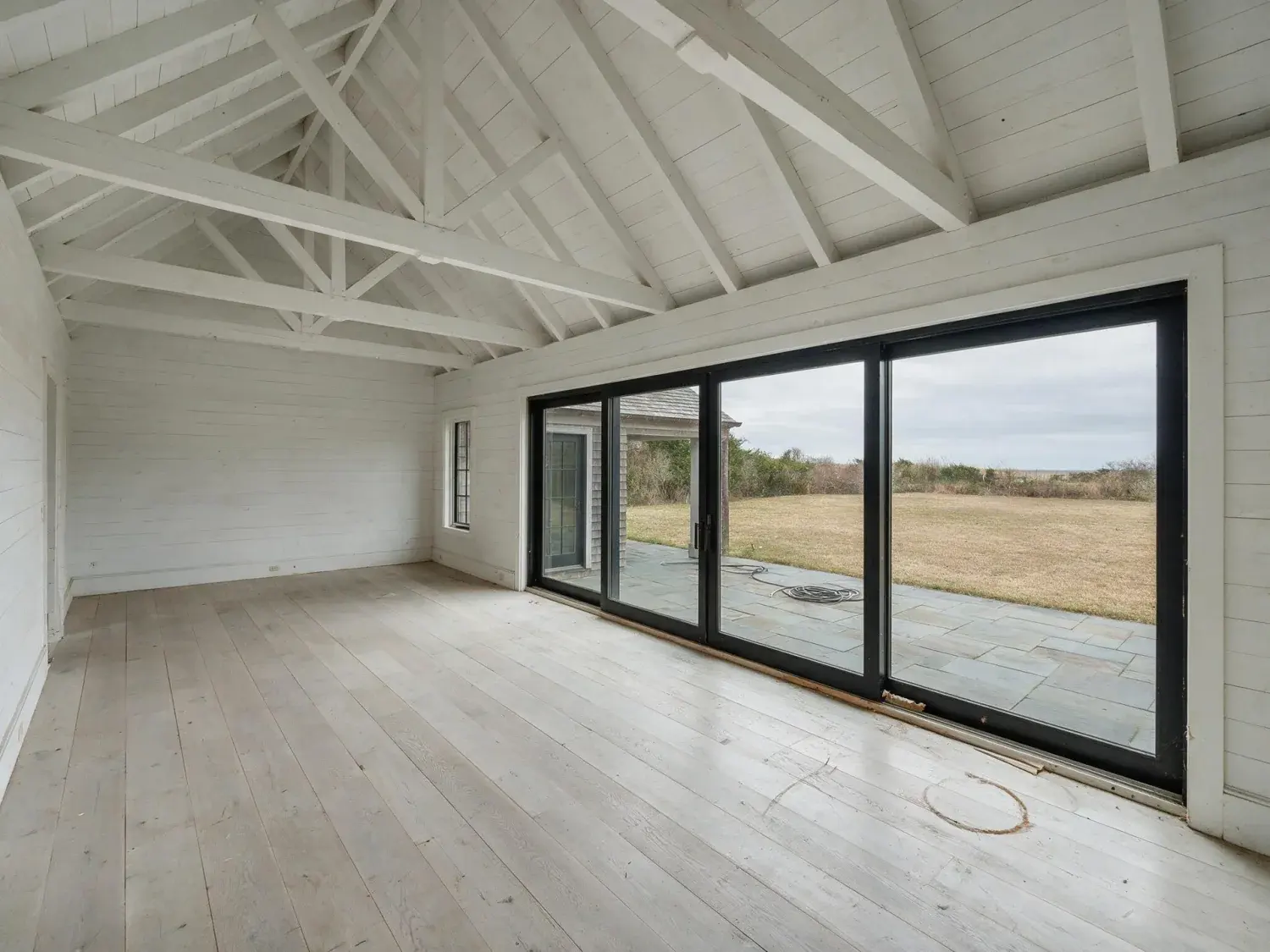 Before and after of a modern bridgehampton barn estate with a cathedral-height great room and sliding glass wall to bluestone patio, staged beyond single-purpose ai-staging tools — original listing photo before editing