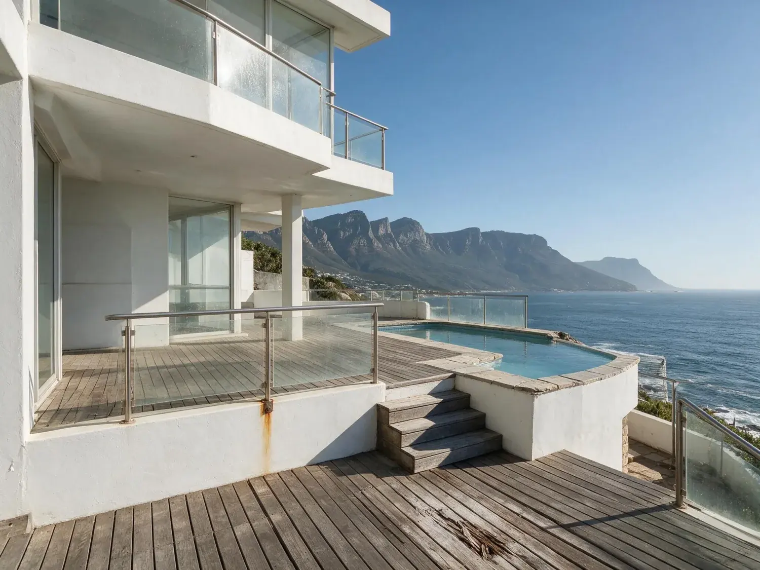 Before and after of a cape town clifton cliffside villa above the atlantic seaboard — white rendered concrete, cantilevered glass decks, infinity pool — preserved exactly — original listing photo before editing