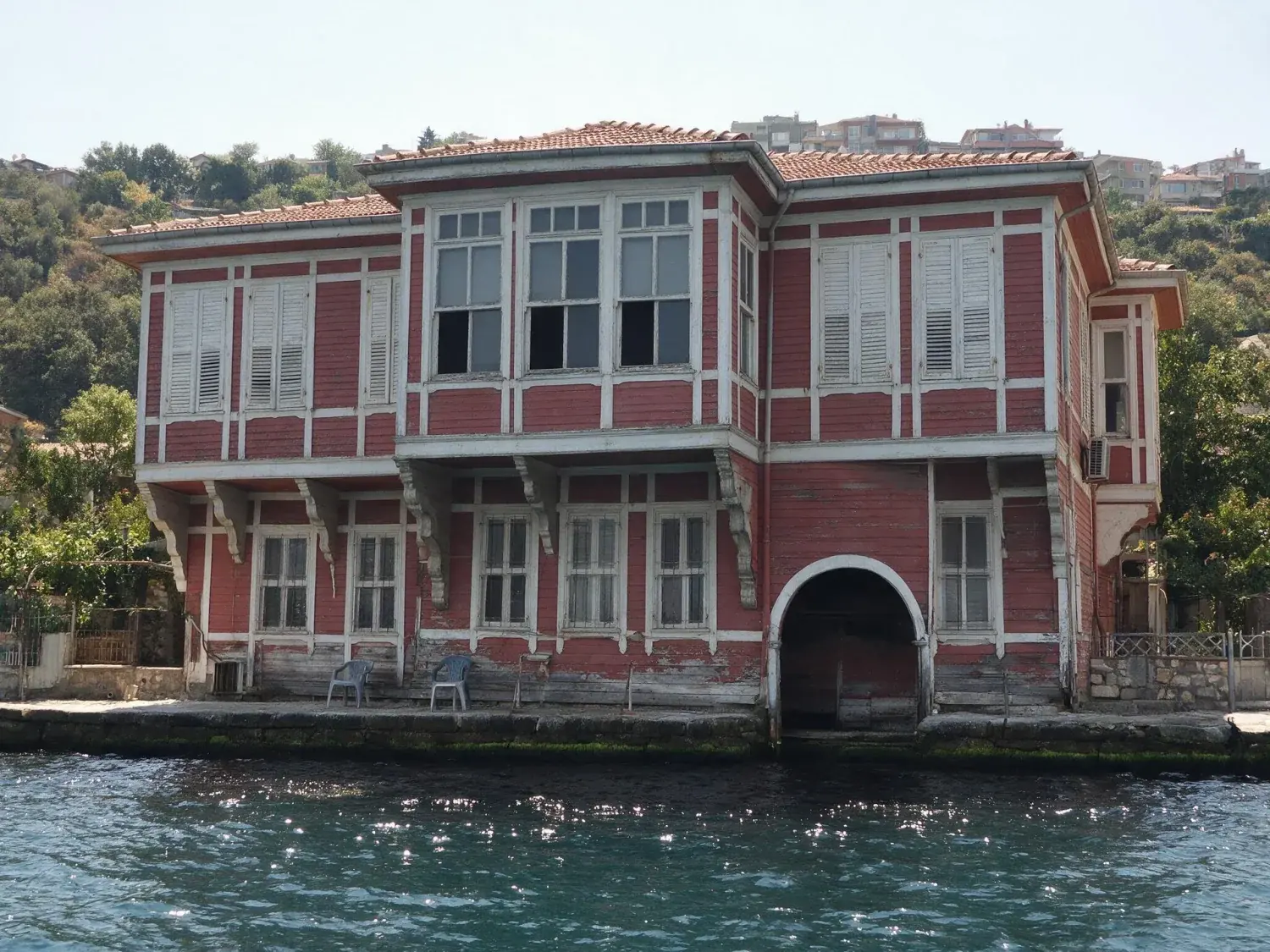 Before and after of a kanlıca yalı shot flat at midday from the water, with every window reading dark — original listing photo before editing