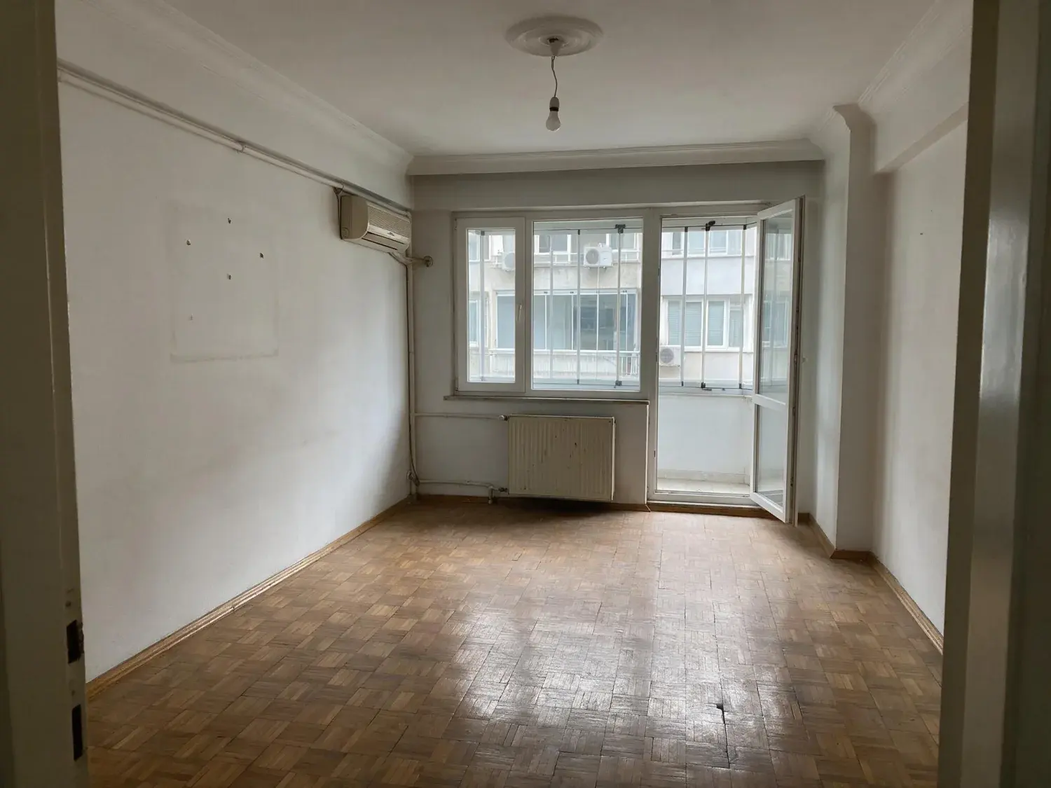 Before and after of a 1970s kadıköy apartman salon the tenants have moved out of, empty down to the bare parquet, furnished for the listing — original listing photo before editing