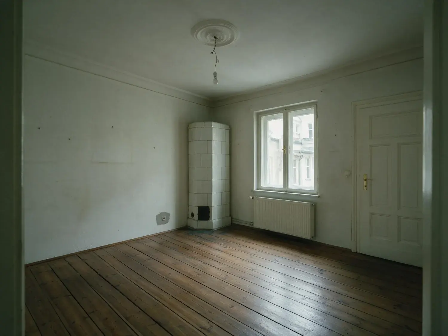 Before and after of an empty berlin altbau room, handed over unfurnished the way they always are, shown as a living room — original listing photo before editing