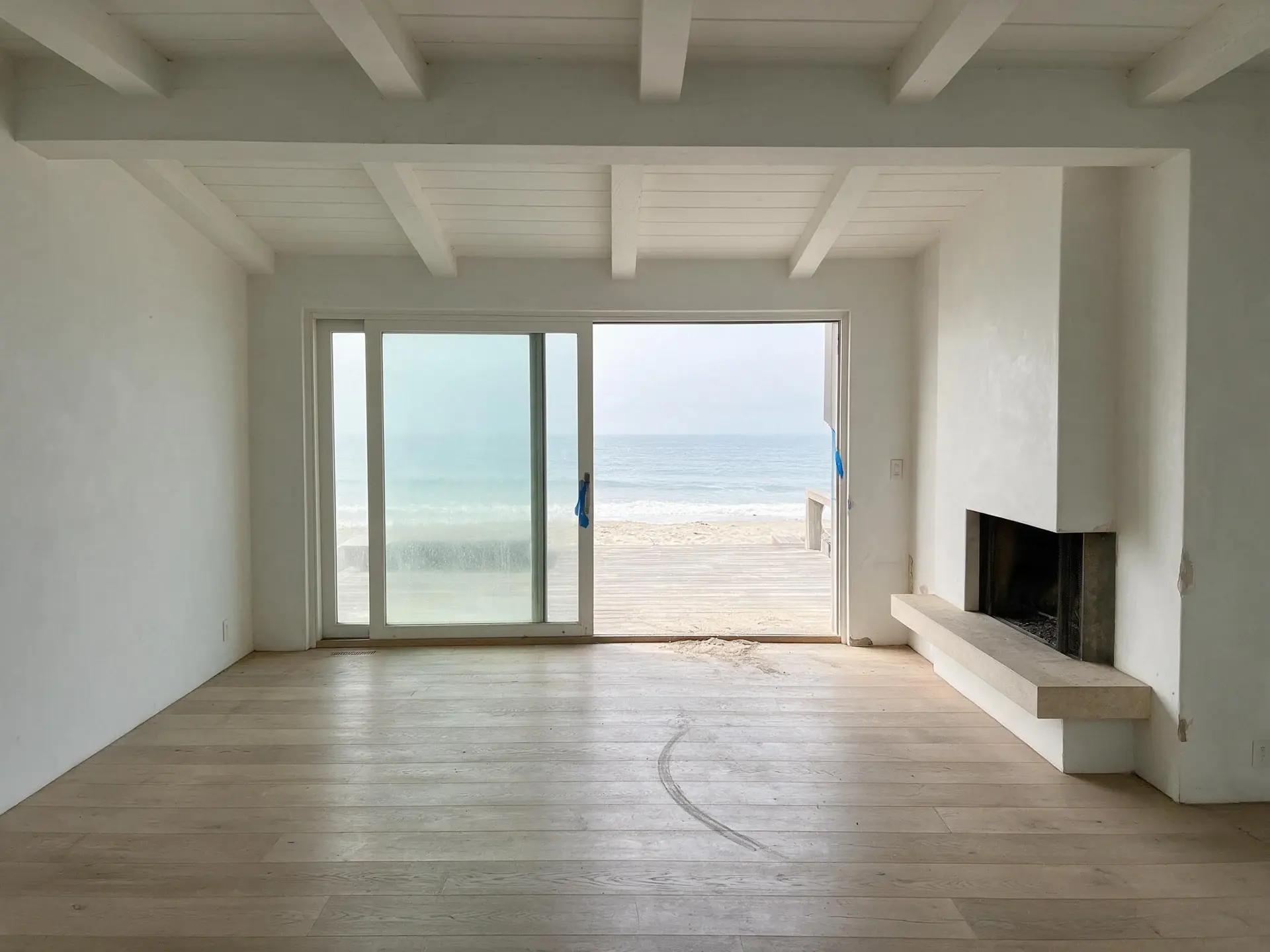 Before and after of an empty oceanfront living room on Carbon Beach, Malibu. — original listing photo before editing