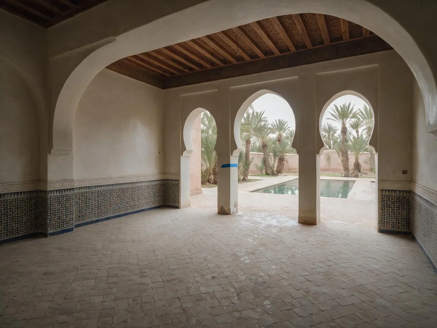 Before and after of an empty riad salon in the Palmeraie, opening to the courtyard pool. — original listing photo before editing