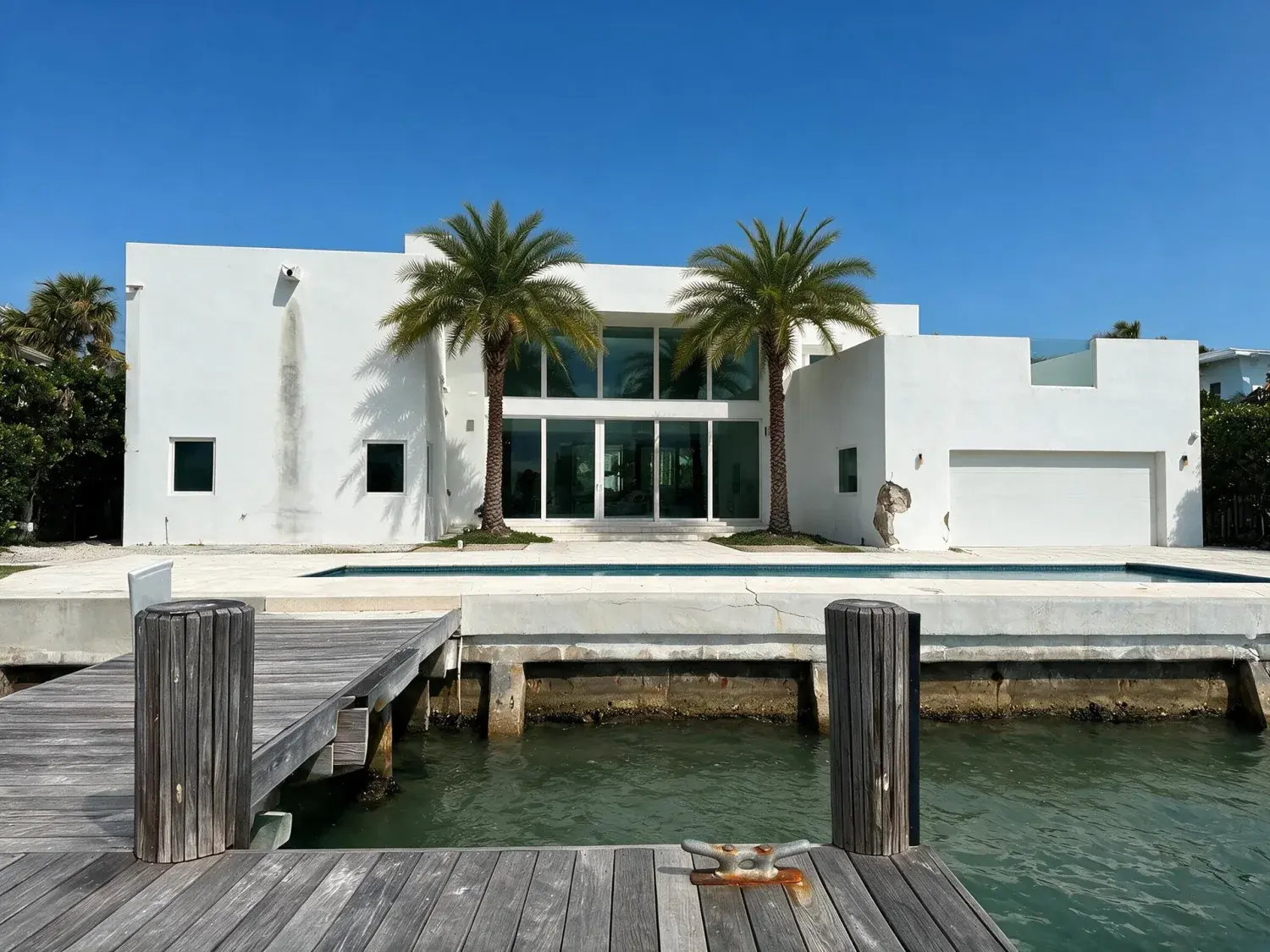 Before and after of a white-stucco miami waterfront modern villa lifted from a stormy grey sky into a postcard tropical azure