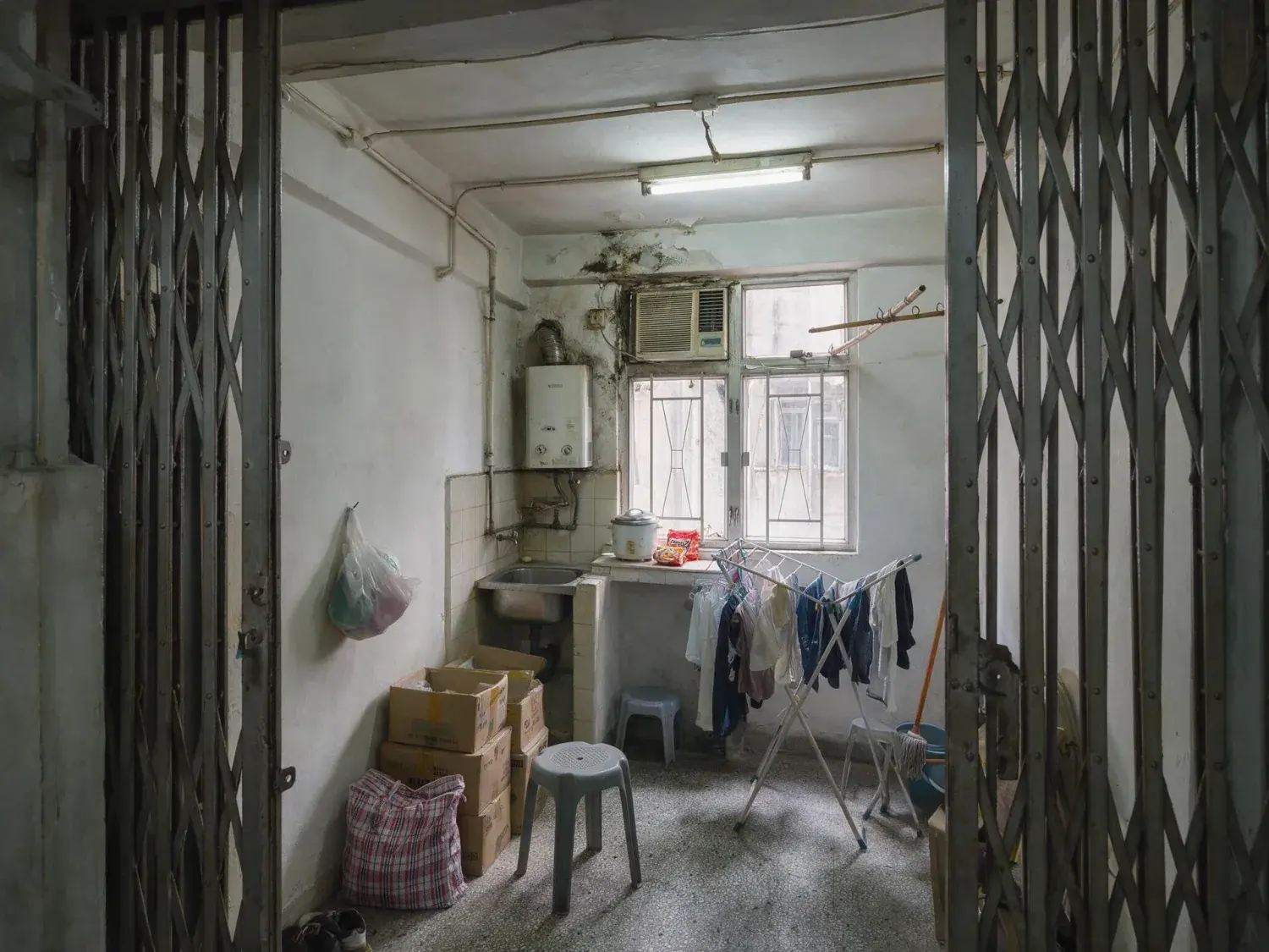 Before and after of a 280 square foot sham shui po flat photographed with the outgoing tenant's laundry rack, cartons and stools still standing in it — original listing photo before editing