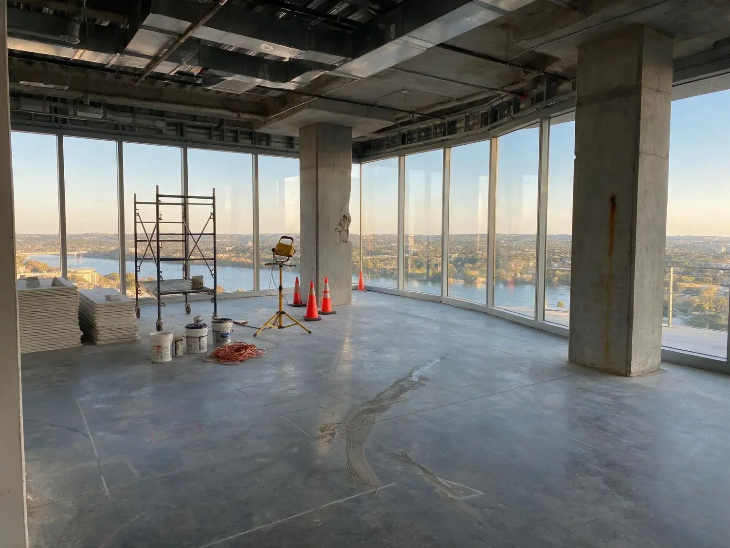 Before and after of a bare austin downtown penthouse shell is renovated into a hill-country-modern residence, keeping the existing lake-and-horizon view intact — original listing photo before editing