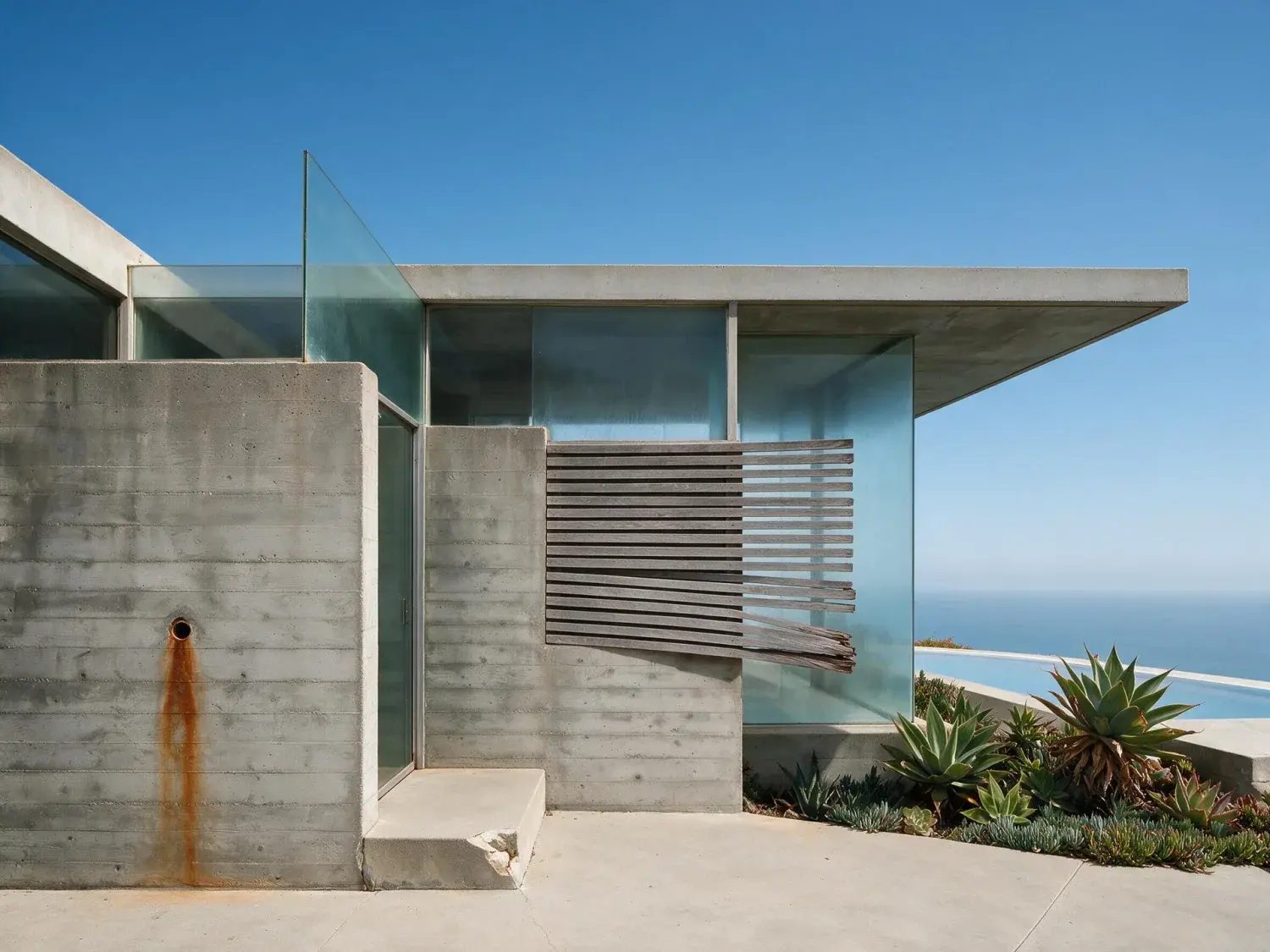 Before and after of a minimalist board-formed-concrete malibu retreat freed from a dull marine-layer sky and given a pacific-blue dreamscape — enhanced by Plotpane