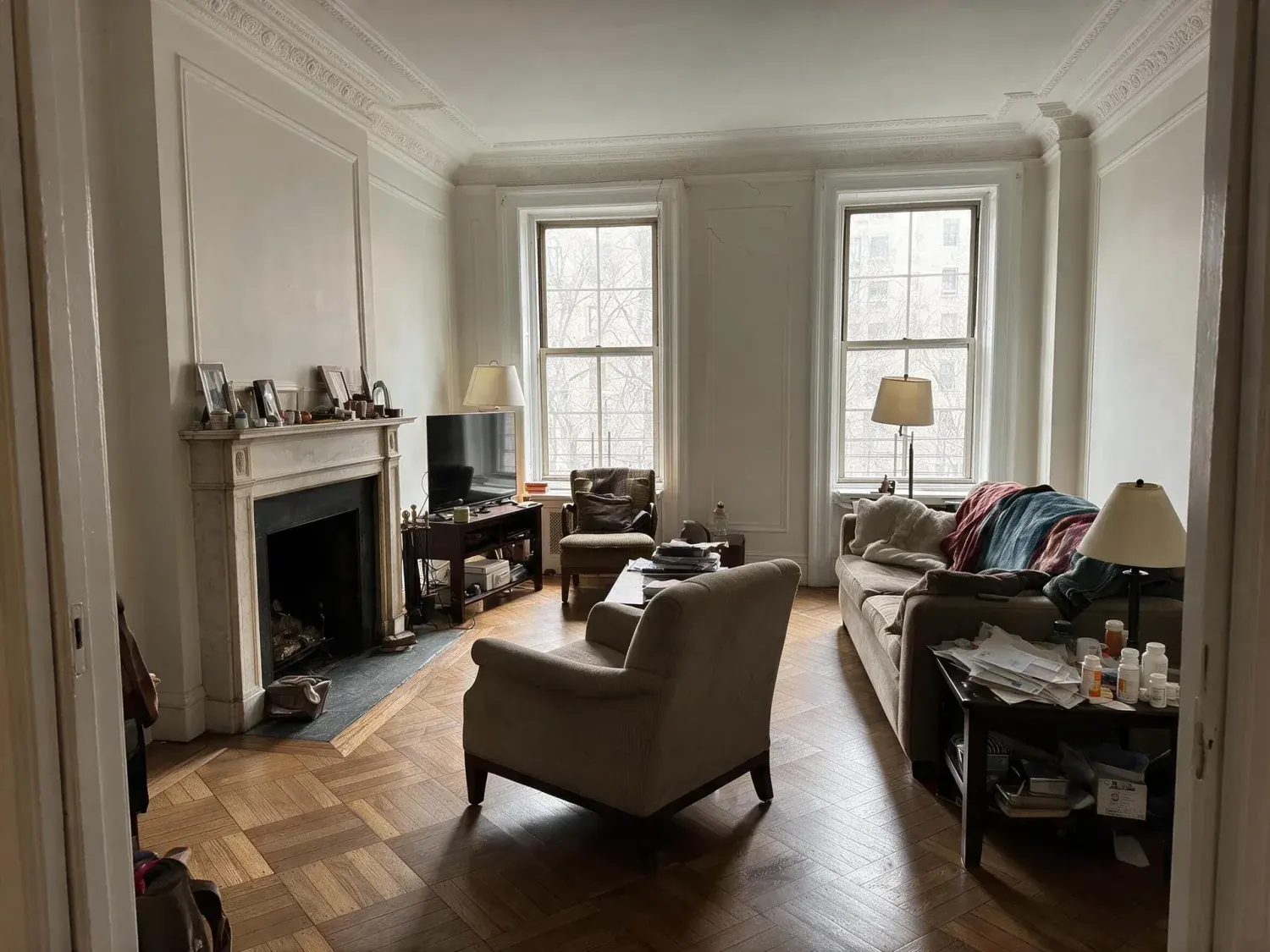 Before and after of a grand prewar park avenue living room with crown moldings and herringbone floors, stripped of a family's lived-in clutter to reveal its bones — enhanced by Plotpane