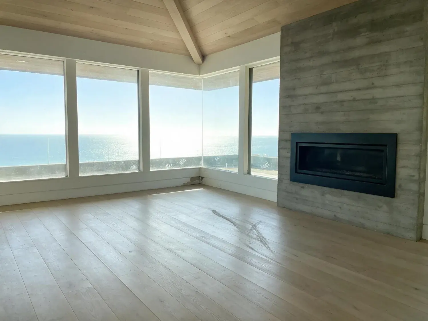 Before and after of a cantilevered malibu glass villa perched over the pacific, the living room an empty sunlit stage waiting to become a buyer's dream — original listing photo before editing