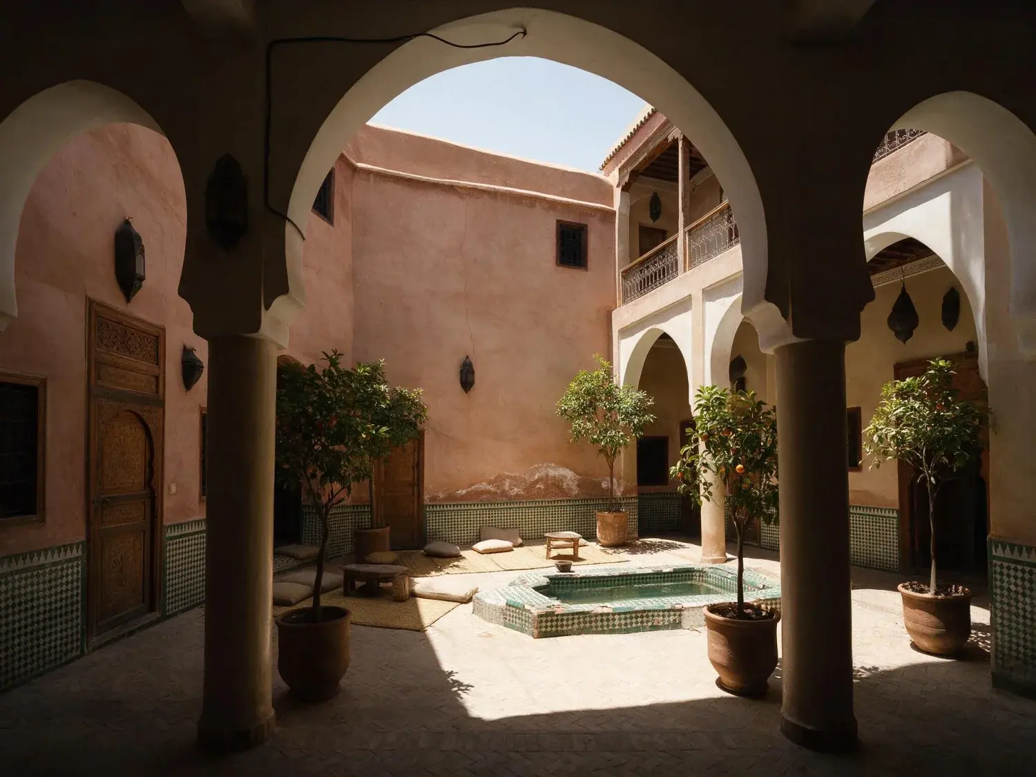Before and after of the courtyard of a medina riad photographed at flat noon, before the lanterns and the guest-room windows are lit — original listing photo before editing