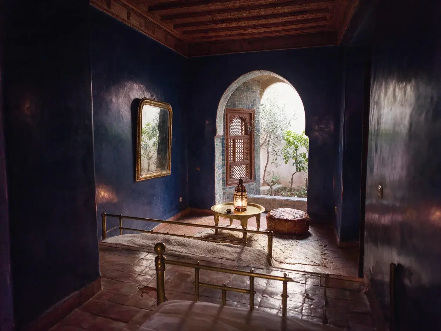 Before and after of a jardin-majorelle-adjacent boutique riad bedroom suite resolves from a muddy underexposure into full zellige and tadelakt colour — distinct from the courtyard riad already in the library — original listing photo before editing