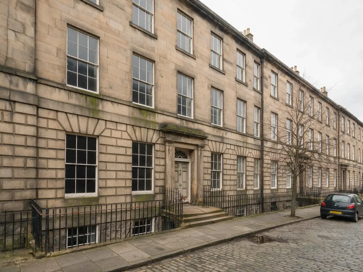 Before and after of a north-facing craigleith-sandstone georgian terrace in edinburgh's new town, captured flat and grey, relit to civil twilight — original listing photo before editing