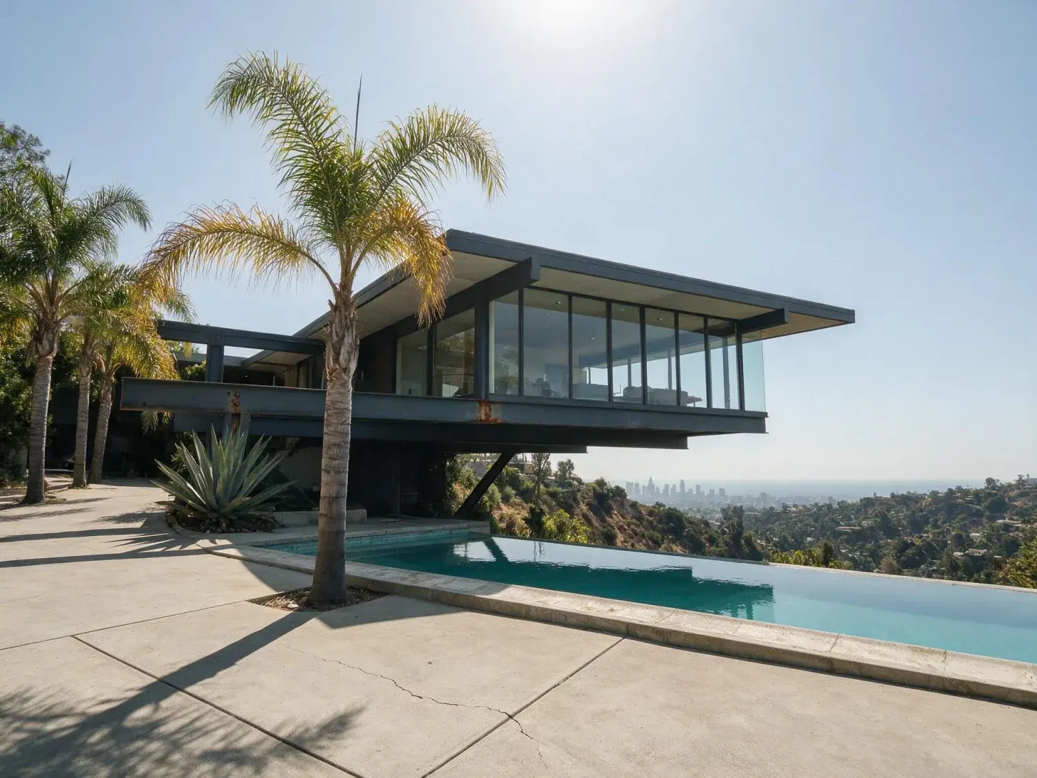 Before and after of a neutra-lineage steel-and-glass cantilever jutting over nichols canyon, transformed from flat midday glare to a cinematic la twilight with downtown skyline glinting beyond — original listing photo before editing