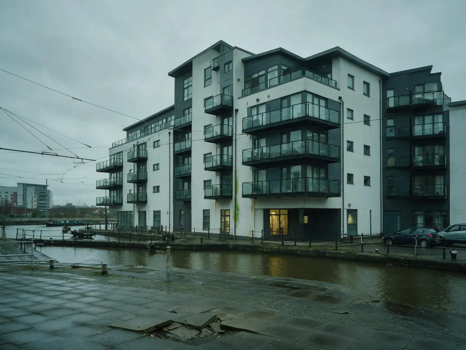 Before and after of a salford quays waterfront modernist apartment block captured under flat pennine overcast — recovered into a rightmove premium hero — original listing photo before editing