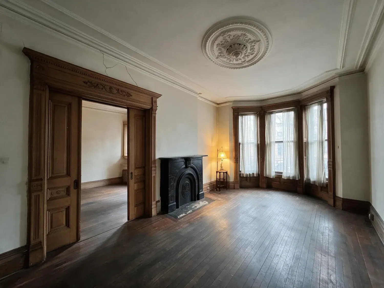Before and after of a stately park slope parlor floor with original plasterwork and pocket doors, pulled from shadowy murk into warm editorial clarity — enhanced by Plotpane