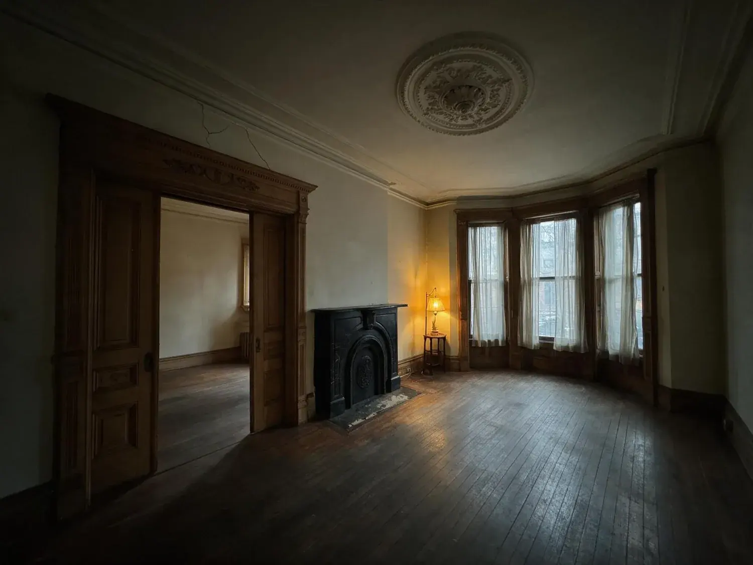 Before and after of a stately park slope parlor floor with original plasterwork and pocket doors, pulled from shadowy murk into warm editorial clarity — original listing photo before editing
