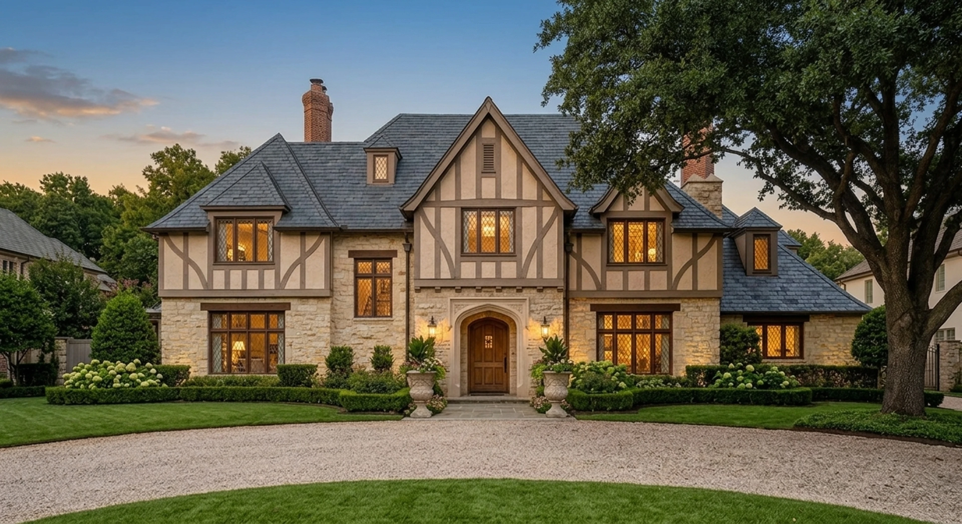 Front exterior of a Highland Park limestone-and-slate tudor estate converted from harsh midday to warm Texas twilight. — enhanced by Plotpane