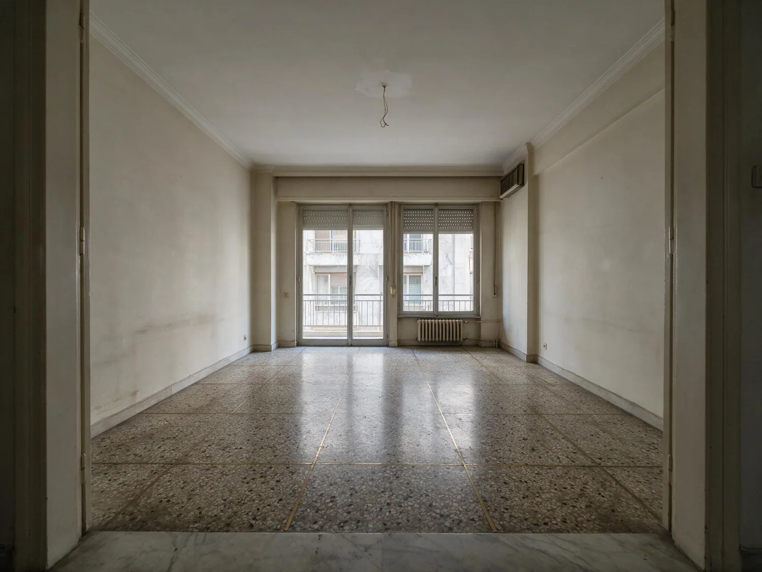 Before virtual staging: empty Athens living room with terrazzo floor, radiators, roller shutters and scuffed walls